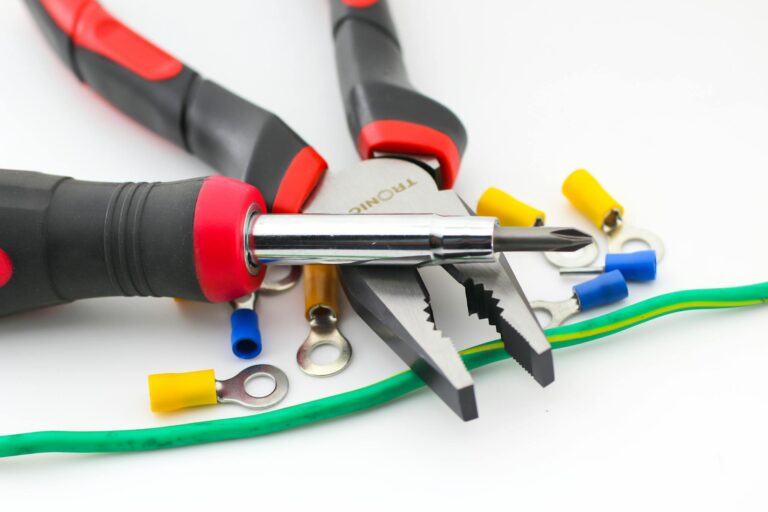 Close-up image of pliers and screwdriver with colorful wire connectors on a white background.